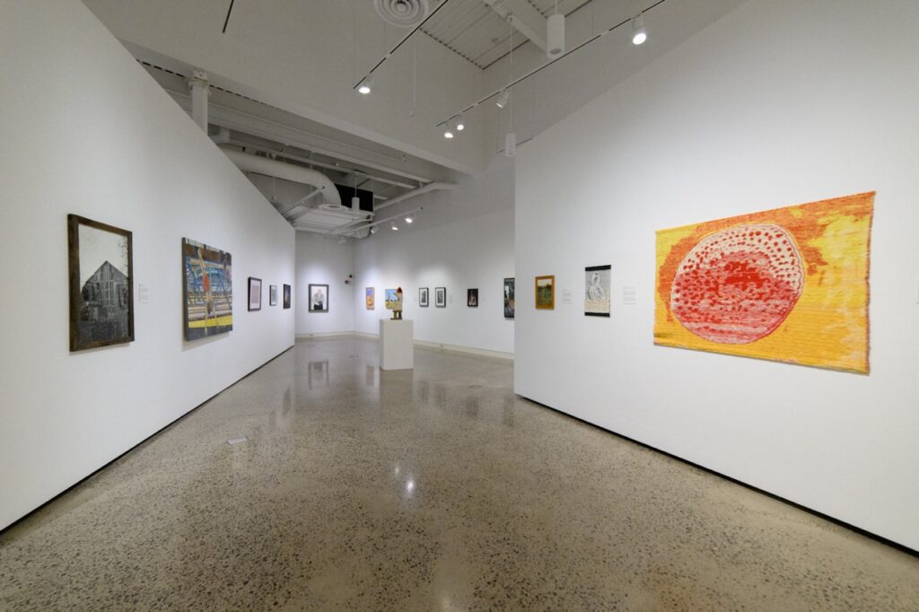 A gallery hall at Erie Art Museum with paintings on white walls.