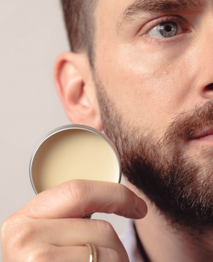 A man holding a natural skincare product from a Pittsburgh shop in a tin next to his face.