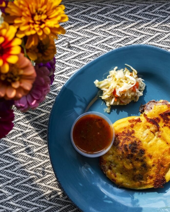 Pupusas on a blue plate on a striped tablecloth.