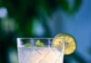 The Best Bottles of Tequila Blanco A glass of tequila blanco sits on a table with a wedge of lime inside and a garnish of lime and mint.
