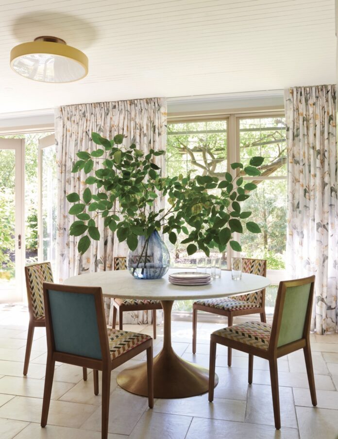 A white dining table with colorful chairs has a potted green plant sitting on top of it.