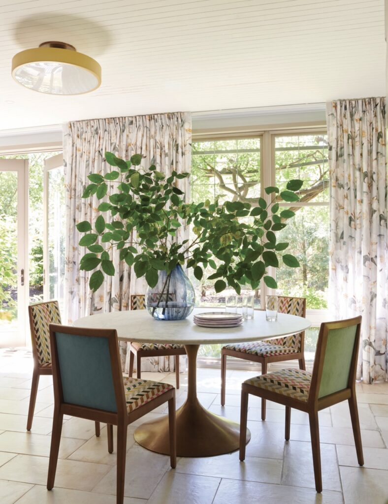 A white dining table with colorful chairs has a potted green plant sitting on top of it.