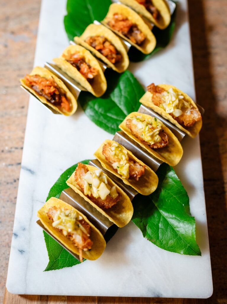Mini tacos from Common Plea Catering sit in a line on top of green leaves.