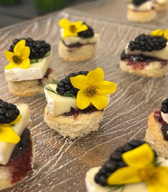 Small dessert bites from Common Plea Catering featuring edible yellow flowers sit on a wood table.
