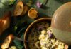 Dandelion Artichoke Dip A brown bowl full of Dandelion Artichoke Dip with a spoon in it and crusty bread laying around the dish.