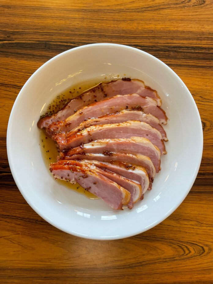 Slices of Easter ham on a white plate on a wood table.
