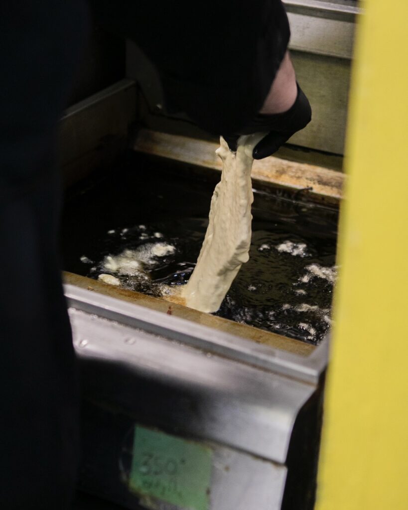 A person drops a piece of fish into a fryer.