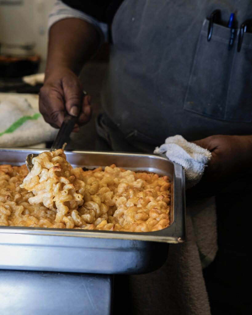 A woman scoops mac and cheese from a pan.