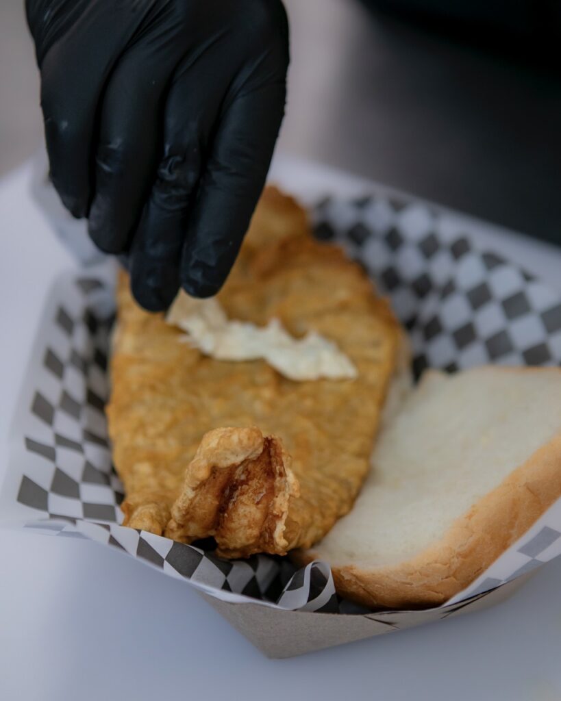 A man pours white sauce onto a piece of fried fish.