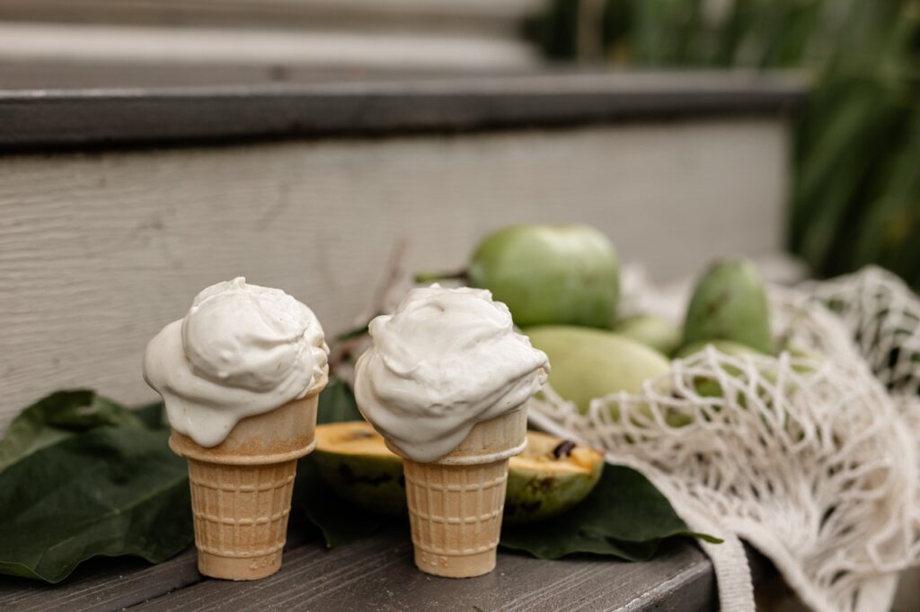 Two pawpaw fruit ice cream cones sit in front of a pile of pawpaw fruits.