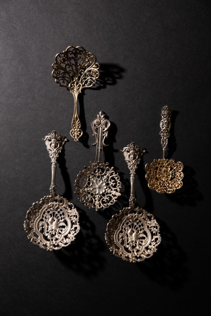 5 gilded bonbon spoons sit in a row on a black table.