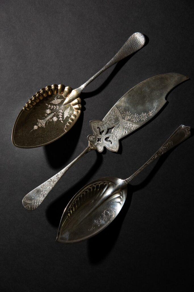 A berry spoon, a fish knife, and a pie server sit on a black tabletop.