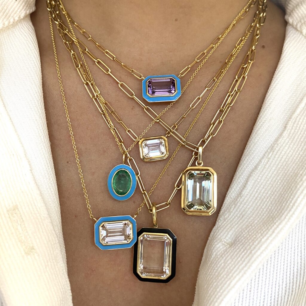 A woman's neck is adorned with various blue, green, and silver necklaces with a white blazer hugging her shoulders.