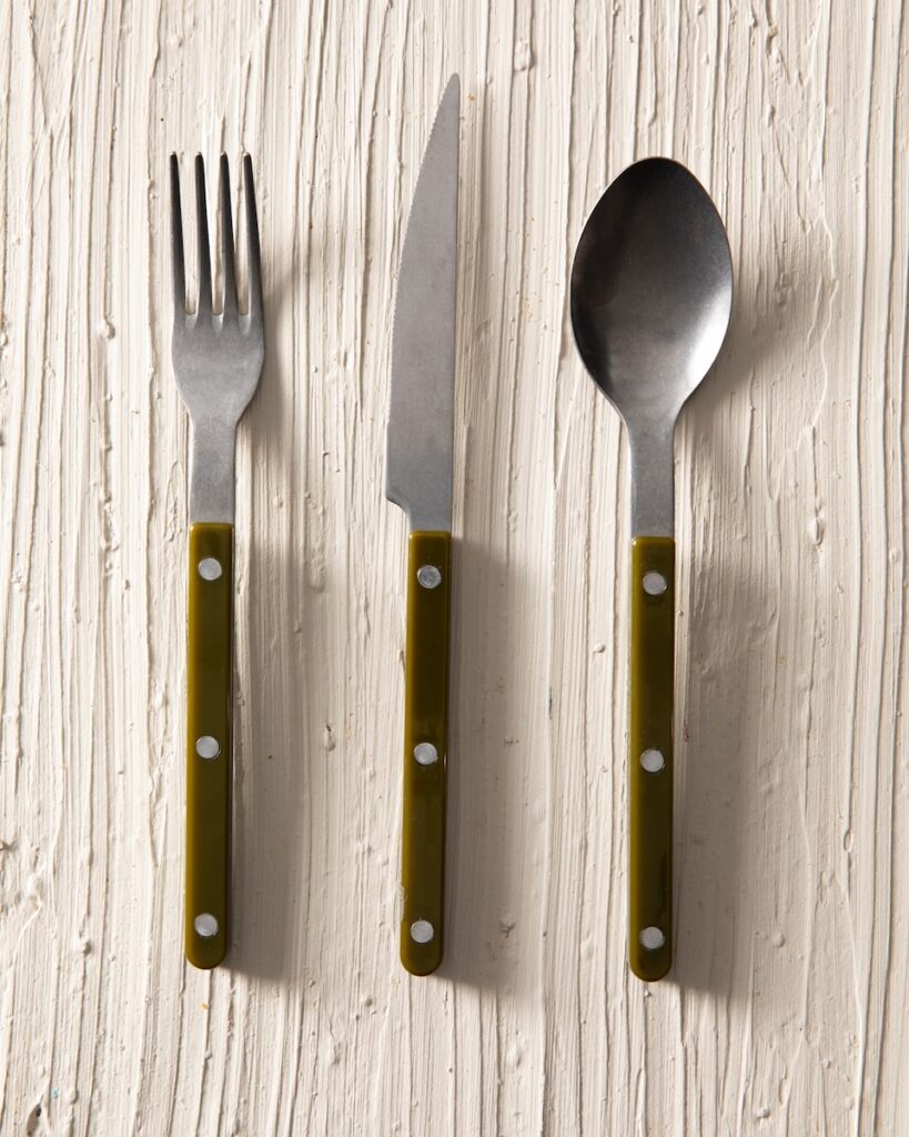 A fork, knife, and spoon in the same set sit on a white table.