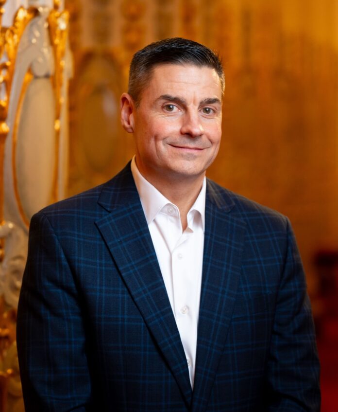 James Santilli with the Pittsburgh Symphony Orchestra stands in a suit jacket in front of a wall in the theater.