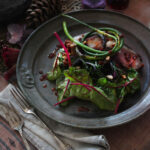 A black plate with a Lamb Rendang on top featuring sauteed greens all on a brown table.
