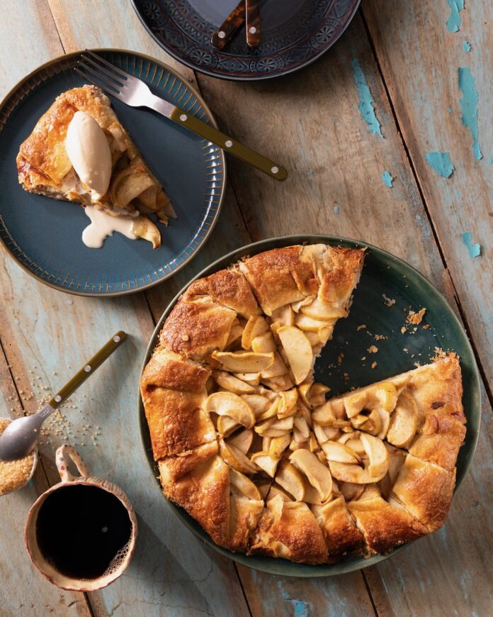 Table-June-8th-web-50 On a dark plate sits an Apple Crostada inspired by Martha Stewart which is made with a cheddar cheese crust. One slice has been cut out and sits on another plate with a scoop of ice cream on top.