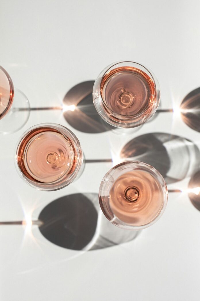 Three glasses of rosé sit on a white picnic table in the sun.