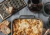 Vegetarian Pasta au Gratin A baking dish with crusty bread sitting around it on a grey table holds a Pasta au Gratin with a spoon scooping out the bottom right corner.