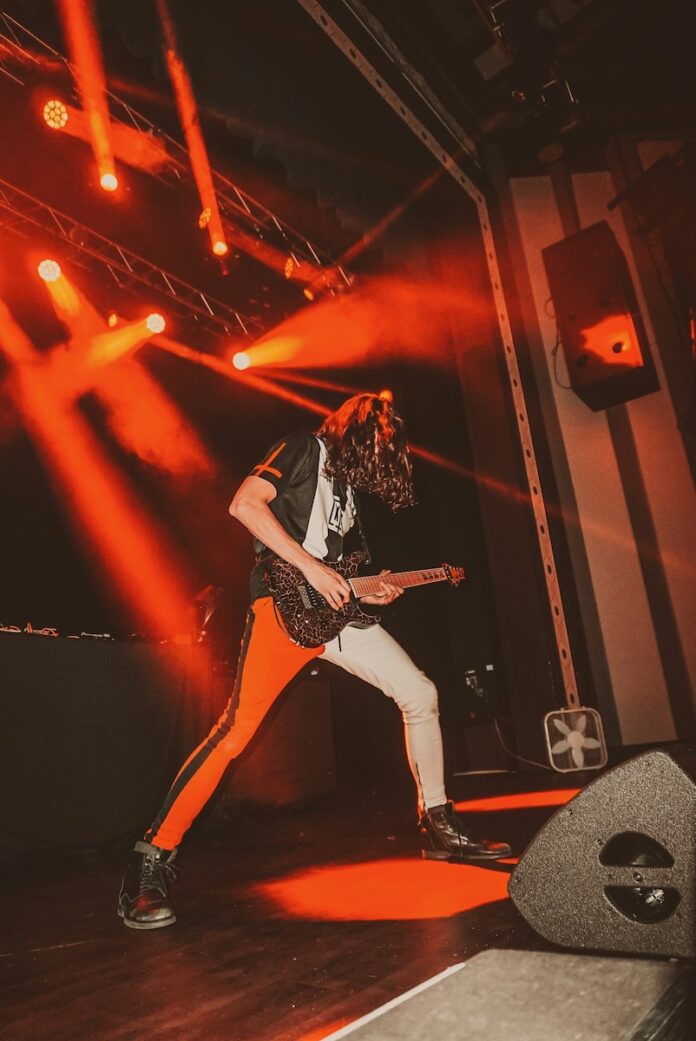 A man plays guitar on stage in Pittsburgh with red lights shining down behind him.