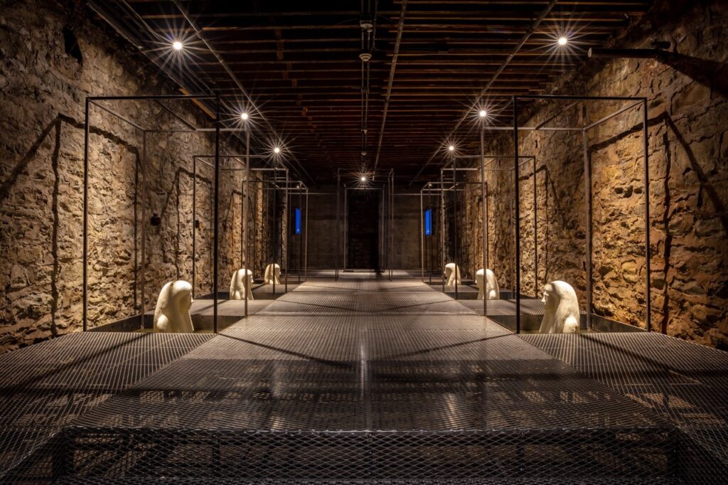 Down a dark corridor are multiple Egyptian statues along stone walls in low lighting.