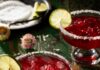 Pomegranate Margarita Two margarita glasses with salt rims are filled with a red pomegranate margarita with a lime wheel garnishing each glass.