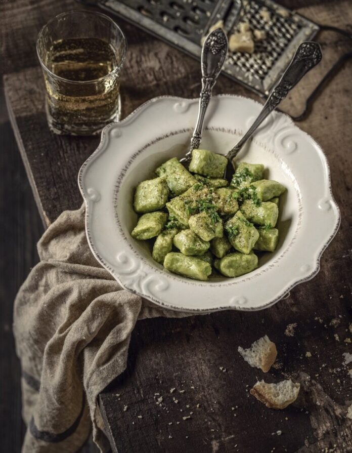 Potato and Sweet Pea Gnocchi A white bowl holds Potato and Pea Gnocchi in a green color with two forks sitting beside the bowl and bread sitting above it.