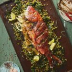 A large Red Snapper lays on a cooking sheet surrounded by a Green Spit Pea Salad and limes in celebration of Nowruz.