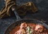 Ricotta Vegetarian Meatballs A bunch of ricotta vegetarian meatballs sit in a cast iron pan, soaked in re sauce with basil garnish on top as the pan is surrounded by pasta, a bowl of the meatballs, and bread.