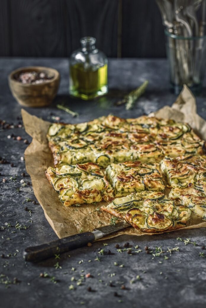 Scarpaccia (Italian Zucchini Tart) A piece of parchment paper sits on a counter top with square slices of Italian Scarpaccia scattered on the paper.
