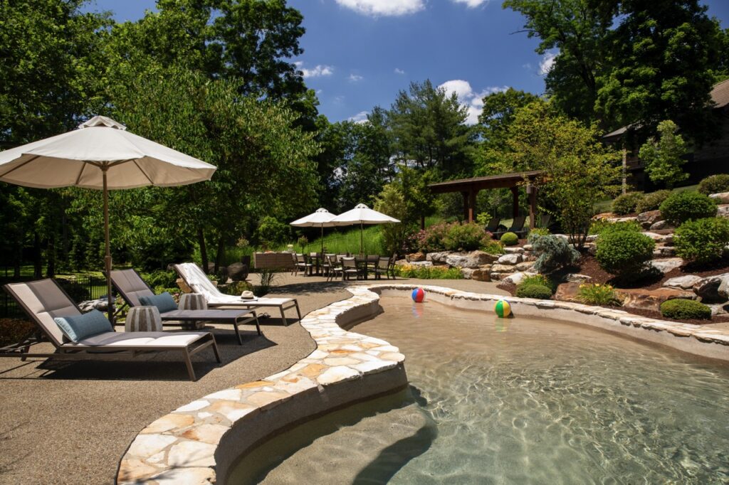 A large pool area with stones along the edge and pool lounge chairs on the deck.