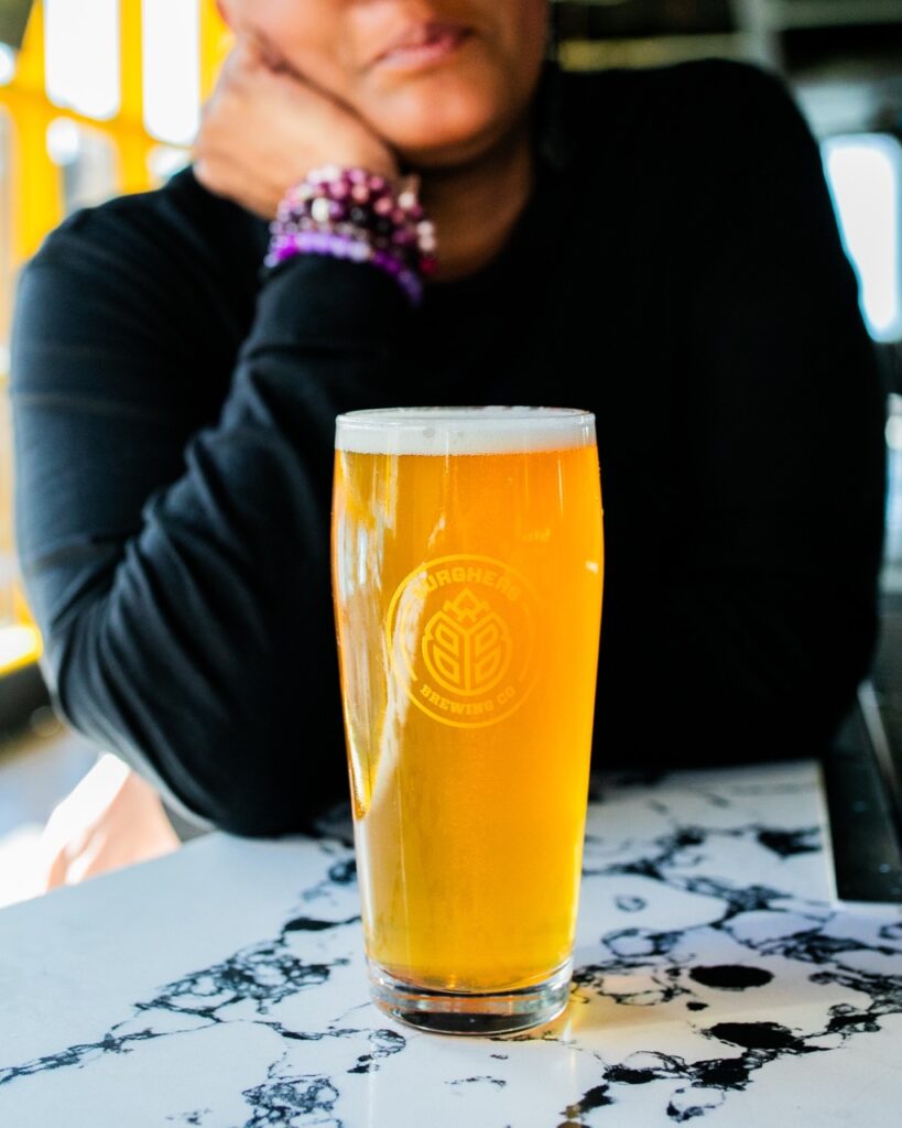 A woman sits behind a glass of craft beer on a marble table.