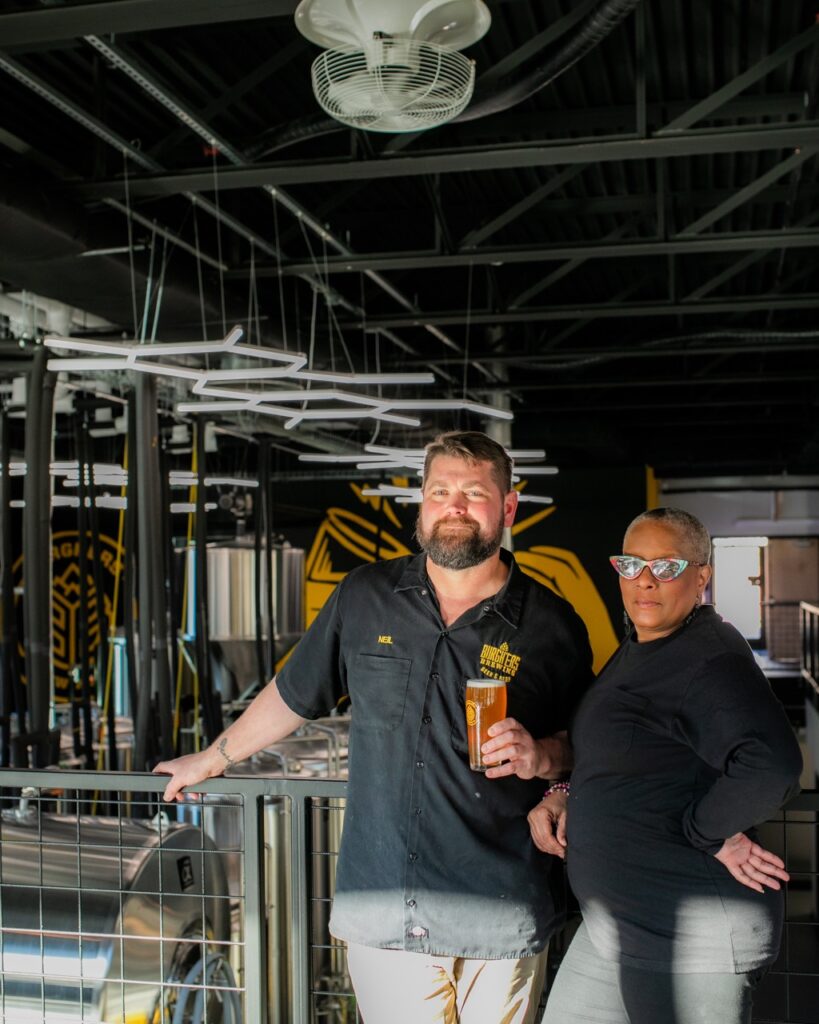 Jackie Page stands beside one of the owner's of a Pittsburgh brewery with a beer in his hand.