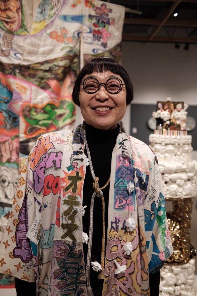 A woman artist in a kimono and black round glasses stands in her art studio.