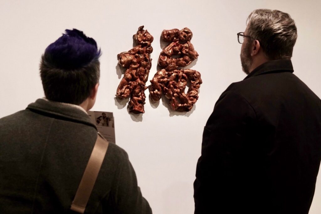 Two people look at a sculpture on a gallery wall.
