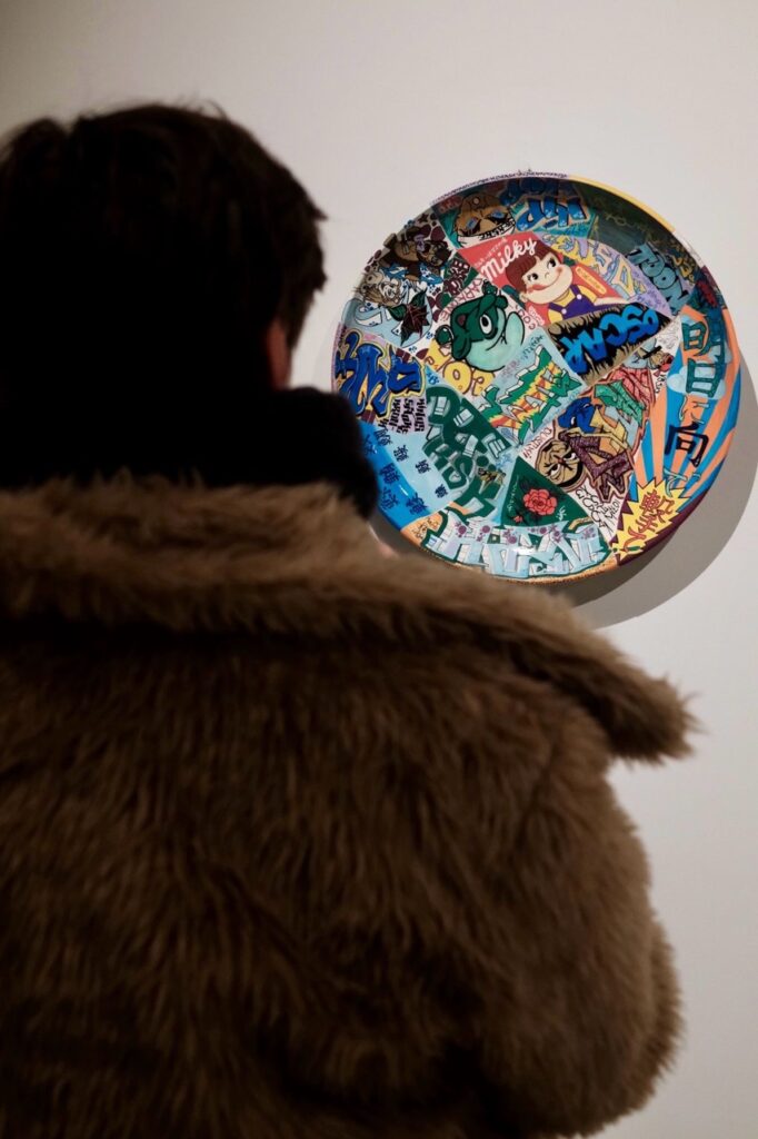A person looks at a painted plate that hangs on a gallery wall.