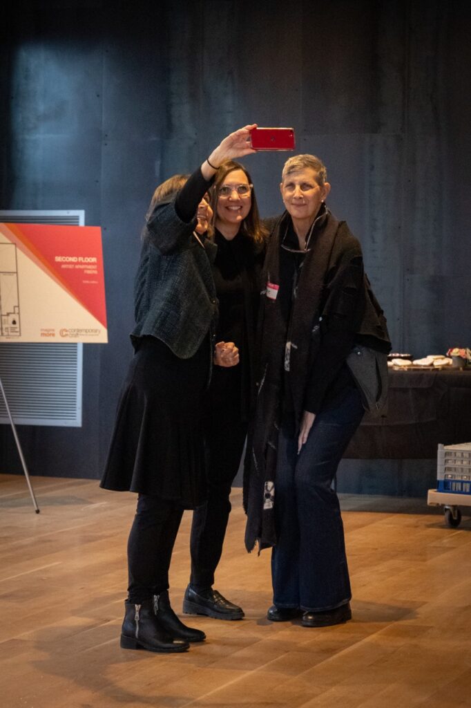 Three women pose together to take a selfie on a red iPhone.