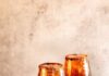 Dark and Handsome (Rum Moscow Mule) Two Dark and Handsome Rum Moscow Mules sit in front of a painted brown background with Tajin rims and a lime and orange sitting next to the glasses.