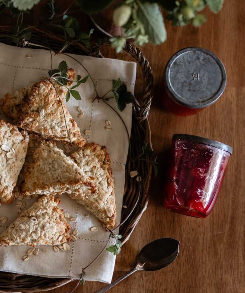 Oat scones and jars of strawberry jam from garden strawberries sit on a wood table.