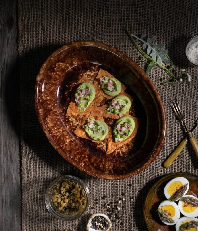 A brown platter holds orange bread squares with a fresh pea puree on top.