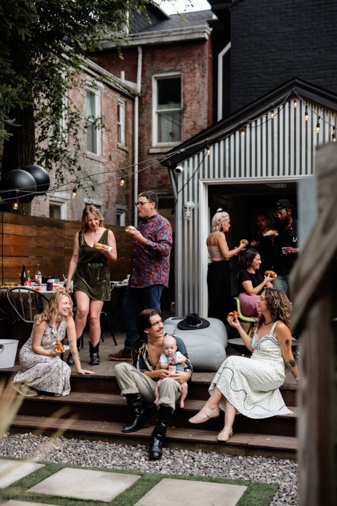 A group of people sit and stand outside a metal tool shed.