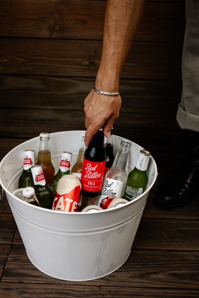A person reaches into a white bucket full of red ribbon soda.