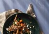 Grilled Lamb Scottadito A green plate holds a grilled lamb legs scottadito with golden fork and knife beneath the plate and a small container of peppercorns on the other side.