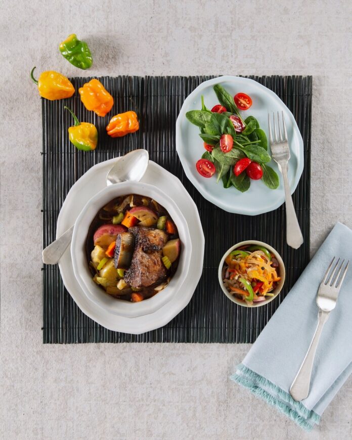 A bowl of soupe joumou on a tablecloth on a white background.