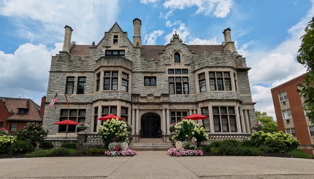 The outside of Mansions on Fifth with a huge mansion building and green bushes with red umbrellas out front.