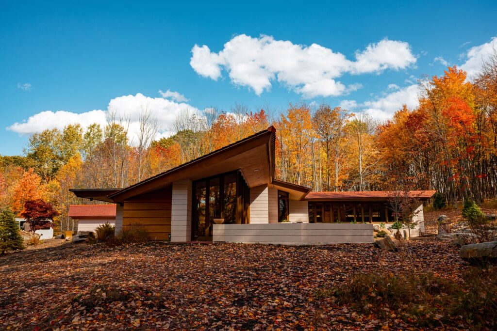 A brown modern lodge in the middle of autumn woods under a blue sky.