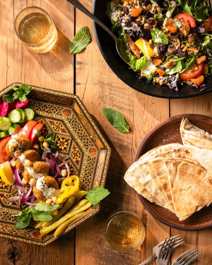 On a brown picnic table sits two plates full of colorful veggies and a small plate of naan from a Pittsburgh international restaurant.