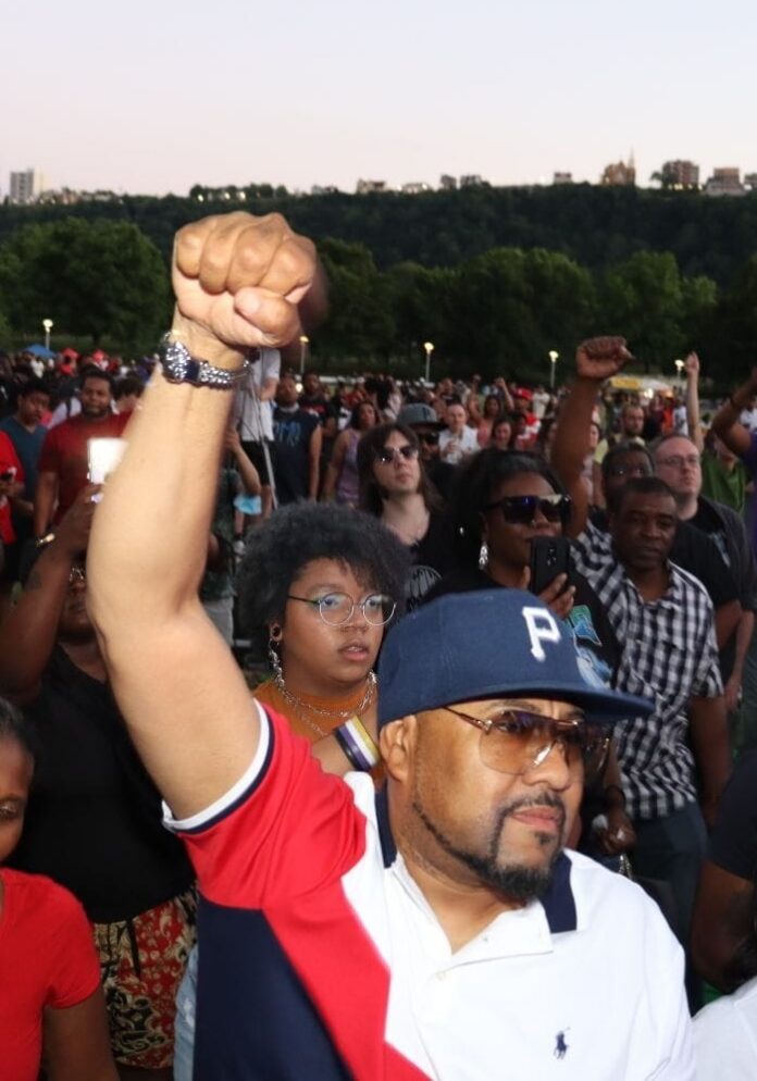 A man in a baseball hat puts his fist up in the air at a Juneteenth concert in Downtown Pittsbugh.