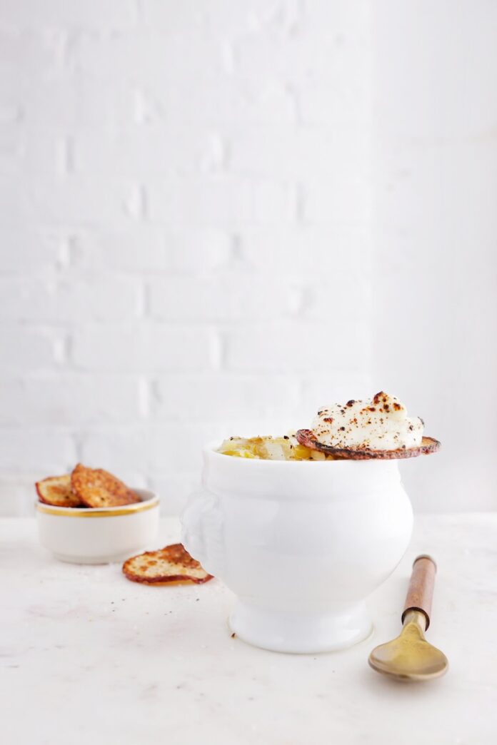 A bowl of potato leek soup with crusty bread on a white background.