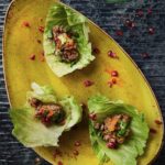 Three lettuce cups with lamb on a yellow plate, staged on a black background.
